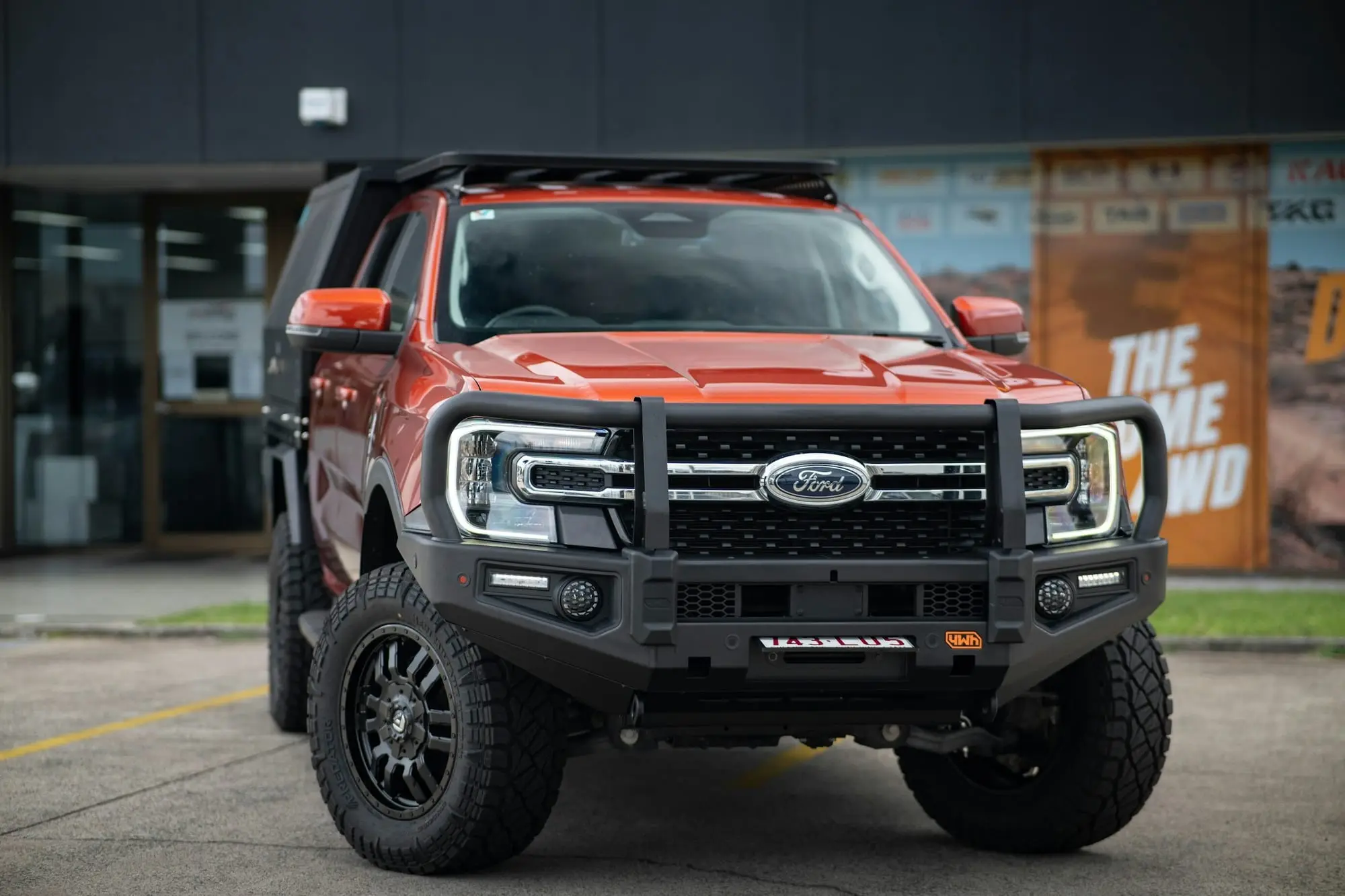 Orange Ford Ranger ute with a bullbar and canopy, front-on outside a 4WD accessories shop