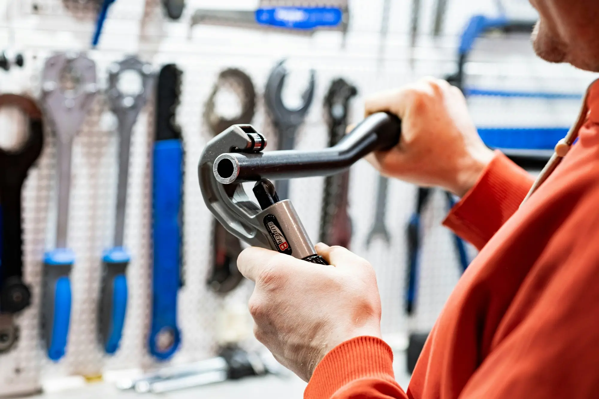 Tradesperson holding a pipe wrench in front of a wall of neatly hung hand tools