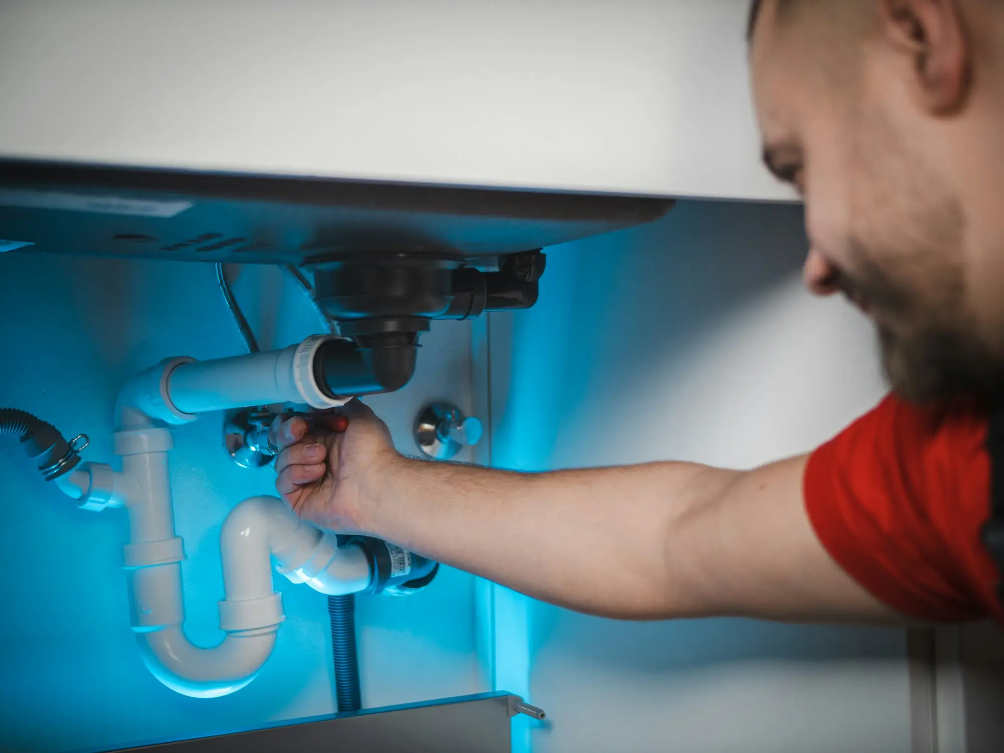 Plumber working on the pipes under a basin with a wrench