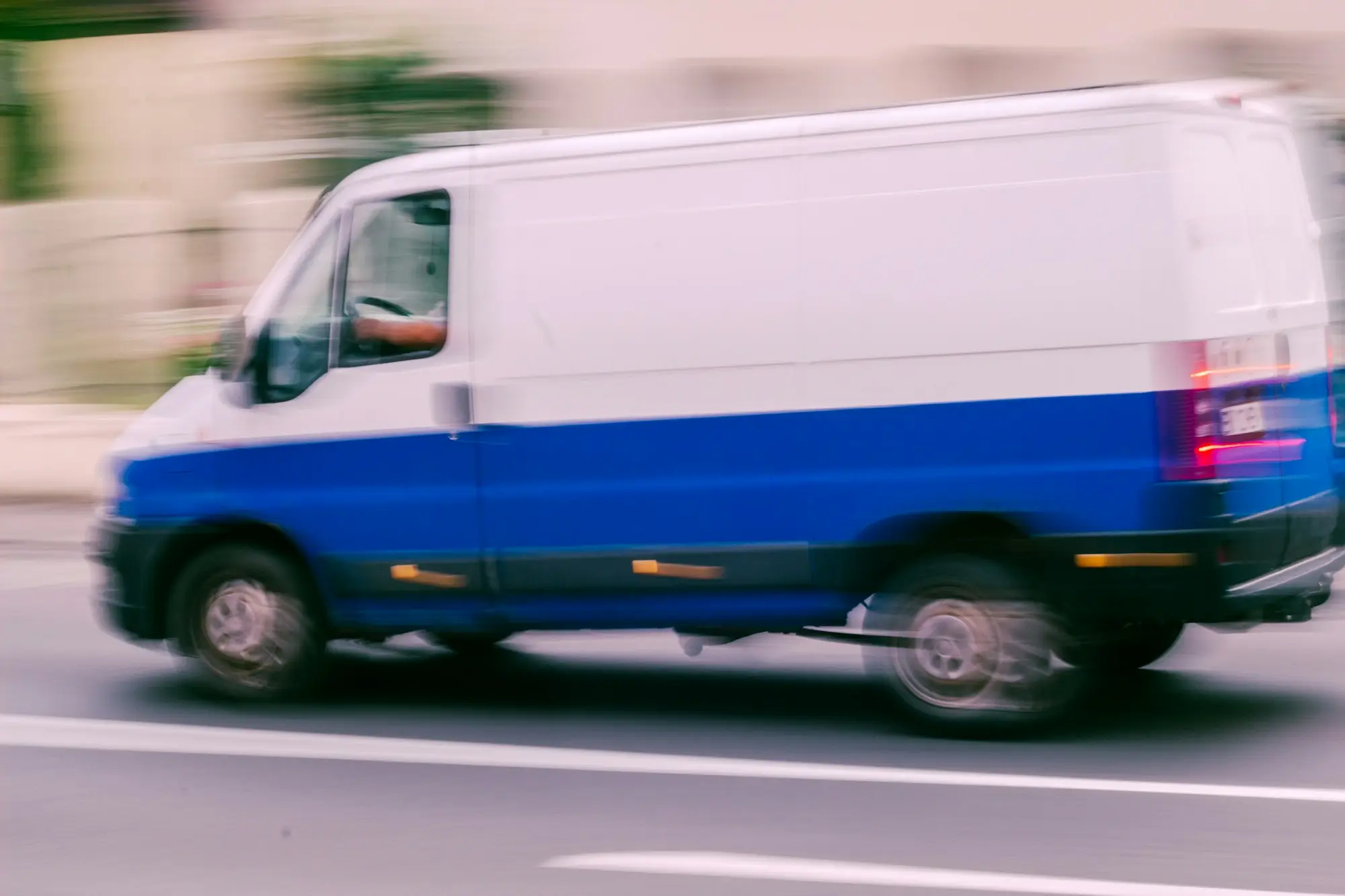 White and blue work van moving along a city street, the kind of vehicle a business needs back on the road after a write-off
